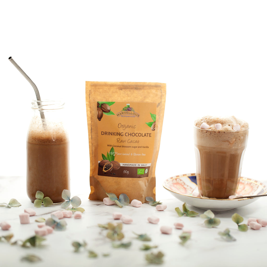 Our organic, vegan and gluten free drinking chocolate in 100% compostable packaging standing next to a cup of frothy hot chocolate.