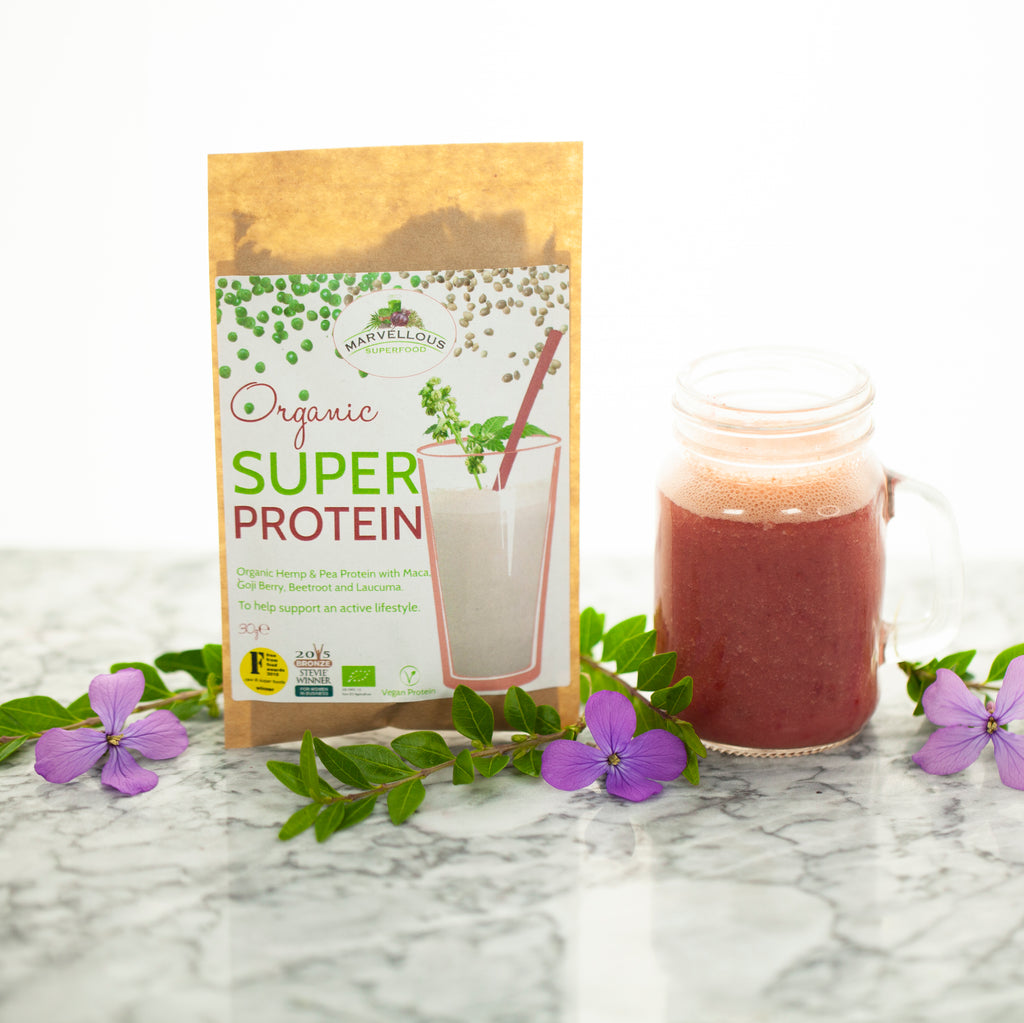Our award winning, plant based, organic Super Protein powder in 100% compostable packaging standing next to a glass of superfood smoothie.